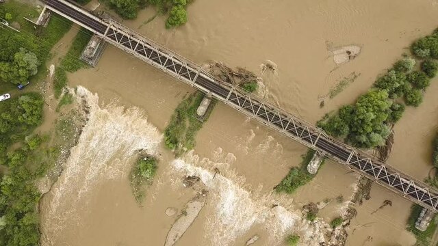 Aerial view of railway metal bridge over dirty river with muddy water in flooding period during heavy rains in spring.