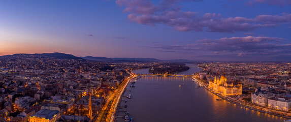 Panoramic aerial drone shot of lighted Hungarian Parliament by Danube river in purple Budapest sunset hour