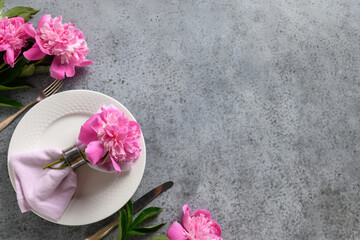 Festive table setting with pink peony flowers, white dishware, silverware on gray. Top view. Space for text.