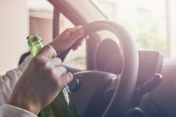 Bottle of beer in a man's hand behind the steering wheel - a concept of driving intoxicated