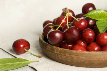 A pile of ripe cherries in a ceramic plate on a wooden table. Red berries of a cherry tree on white.
