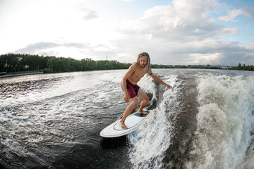 young sports man wakesurfer with dreadlocks ride the waves on surfboard.