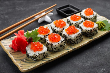Sushi roll with red caviar on a plate with wasabi, ginger, maple leaves and chopsticks for sushi, on a black background