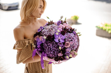 attractive woman holding bright bouquet of different flowers of purple colour