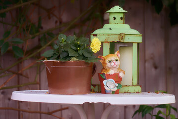 cute decorative cat figure with solar light stands on a garden table next to a vintage green lantern and a flower pot