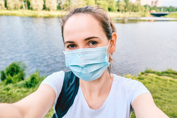 Portrait of a Caucasian woman in a medical mask during a pandemic in the city makes a selfie photo....