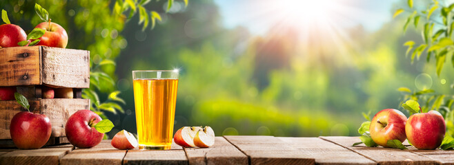 Apple Crate And Glass Of Juice On Wooden Table With Sunny Orchard Background - Autumn / Harvest Concept
 - obrazy, fototapety, plakaty