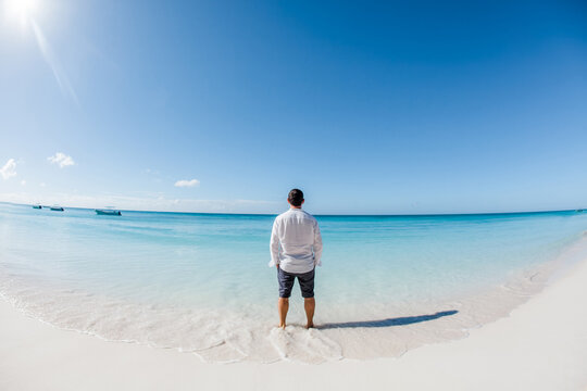 Man standing on caribbean beach enjoying the view of tropical landscape with white sand, blue water and palm trees jungle at Saona island in Dominican republic. Freedom concept
 