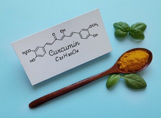 Structural chemical formula of curcumin molecule with wooden spoon filled with turmeric powder (curcuma). Turmeric is an old Indian spice with a powerful medical compound called Curcumin.