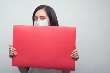 Caucasian female in a face mask holding a red rectangular sign with space for your text on it