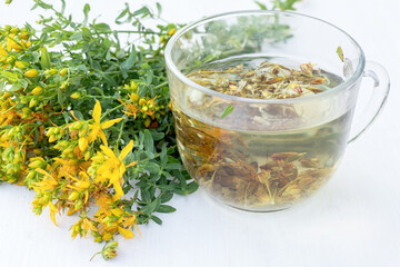 Transparent cup of St. John's wort remedy beverage with bunch fresh Hypericum yellow flowers. jar of spring honey. Medicinal herbs for Alternative Medicine and Homeopathic Remedies