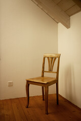 Wooden Chair in a corner. Wooden Floors and beams from the ceiling exposed. Antique. Classic.