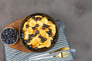 Trendy home breakfast with tiny pancakes and blueberry on gray concrete background. Flat lay, top view, overhead, mockup, template, copy space. View from above. High quality photo