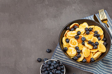 Trendy home breakfast with tiny pancakes and blueberry on gray concrete background. Flat lay, top...