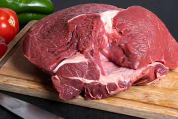 .rump on a cutting board with a knife beside it with red pepper and green pepper in the background