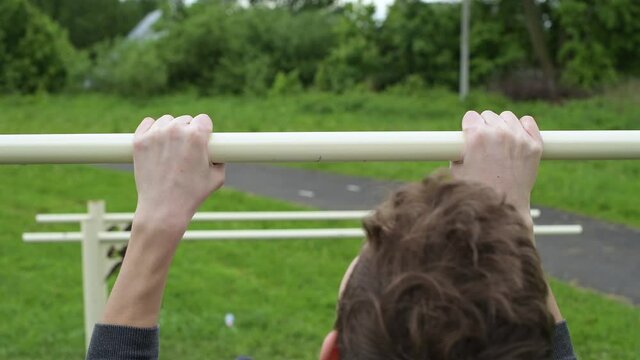A teenager hangs out on a horizontal bar and unsuccessfully tries to pull himself up. Guy training outdoors
