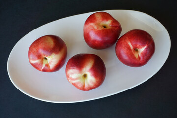 Fresh red nectarines, a beautiful, appetizing dessert, on white plate, black background.