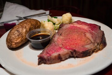 This close up image shows a delicious, fine dining prime rib meal with sides of baked potato and vegetables.