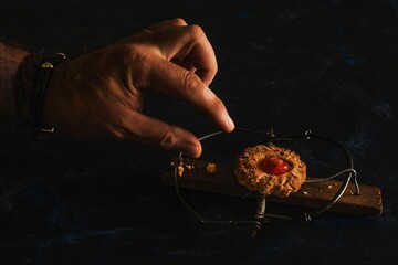 Closeup shot of a hand reaching for a jam cookie in a mousetrap on a black table