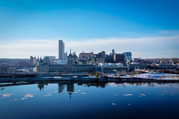Fototapeta na wymiar Albany NY skyline on a winter day seen from across the calm and reflective hudson river with ice floating in the river