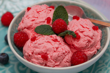 
three balls of raspberry ice cream with three leaves of mint and berries in a bol very close-up.