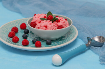 
raspberry ice cream in a blue plate with blue gauze on a blue background, closeup side view.