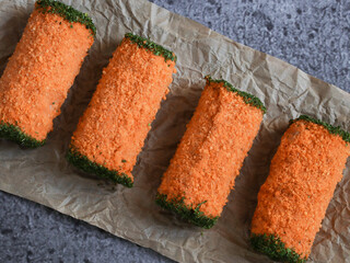 
three minced meat rolls in bright orange breadcrumbs and greens at the edges on a stone background, close-up top view.