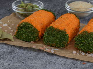 three minced meat rolls in bright orange breadcrumbs and greens at the edges on a stone background, closeup side view.