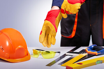 Construction worker putting on protective gloves. Composition with safety equipment and tools. Copy space.