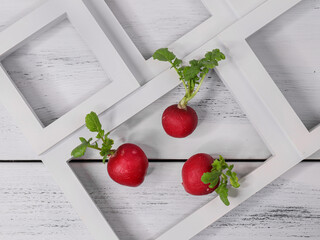 three red radishes in a white frame on a white wooden table, top view close-up.