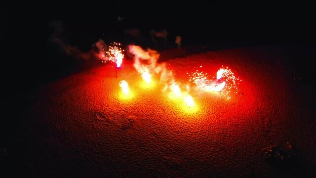 Firework burning outside on the beach - red fireworks spinning around and spreads sparkles around
