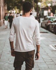 Back view of a male with a white long sleeve t-shirt walking on the sidewalk