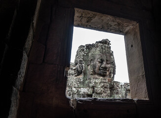 Rosto da estátua visto por uma janela em templo do Cambodia. 