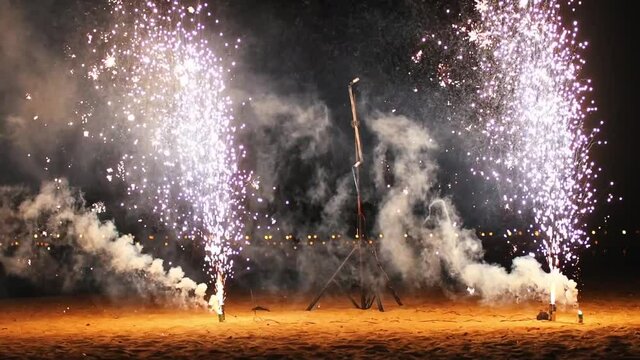 Small white firework burning on the beach of a night city and produces smoke