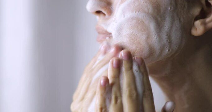 Woman is washing cleaning face with organic foamy soap cleanser, closeup view. Girl is cleansing her face skin, making massage movements. Beauty procedure, spa, wellness and healthy skin care concept.
