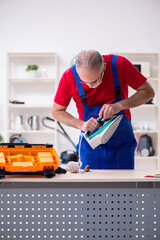 Old male contractor repairing iron indoors