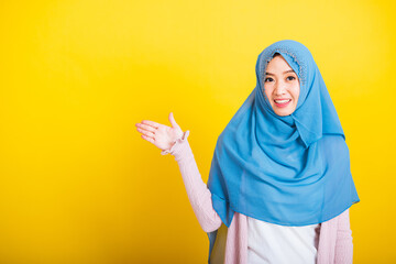 Asian Muslim Arab, Portrait of happy beautiful young woman Islam religious wear veil hijab funny smile she positive expression open palms with something on hand side space isolated yellow background
