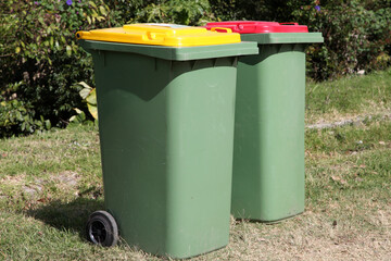 Rubbish and recycling bins on the side of a road with plants and trees in background