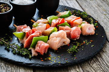 Uncooked shashlik and seasonings on black stone board on wooden table