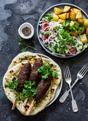 Meat kebab, garlic tortillas naan, yogurt dressing vegetable salad, baked potatoes - delicious lunch, tapas in the mediterranean style on a dark background, top view.