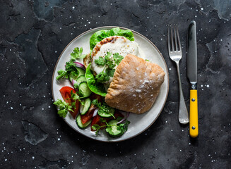 Ciabatta roll bread sandwich burger with chicken cutlet and mayonnaise mustard sauce and vegetables salad on a dark background, top view
