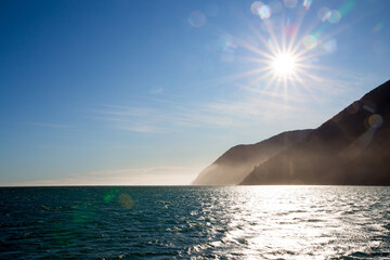 The cruise boat  goes out through the fiord from Milford Sound to the Tasman Sea where the sea is calm and the sun glistens on the ocean in winter, New Zealand