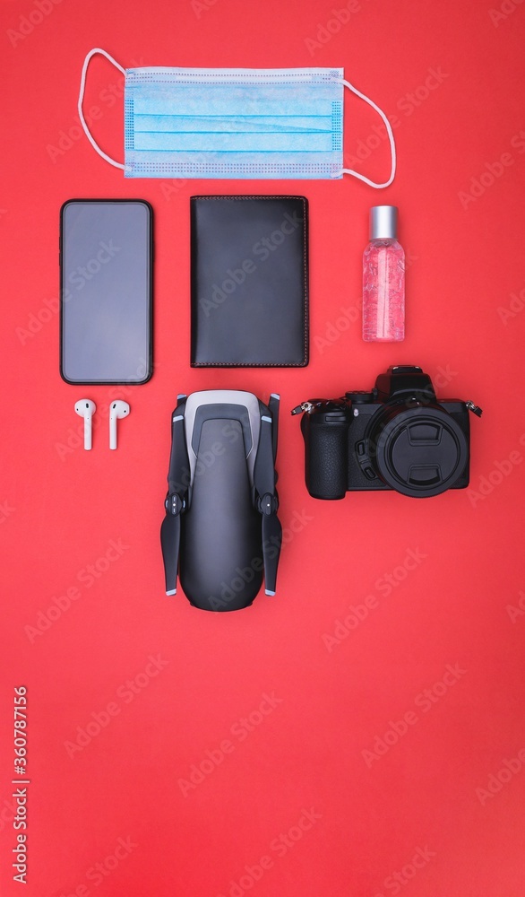 Canvas Prints a mask, hand sanitizer  smartphone, ear pads, passport holder, camera and drone on red background