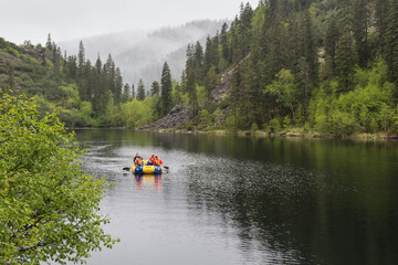 Landscape with a beautiful mountain lake among the mountains covered with coniferous and deciduous trees in foggy weather. An inflatable boat is floating on the lake