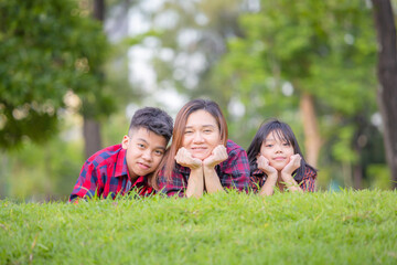 Smiling Mom and two children lying on grass, Happy mother son and daughter in a park, family concept