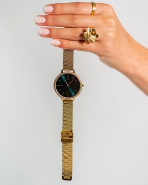 Vertical Shot Of A Woman Wearing Two Rings Holding A Gold Watch N Front Of A White Background