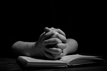 Two hands on a book. A man prays in the dark. Bible.
