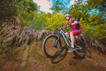 Young caucasian male jumping with a mountain bike over a wall ride. Epic ride with a modern mountain bike on a trail park.
