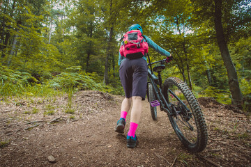 Naklejka premium Back view of an unknown woman pushing a modern mountain bike up on a singletail park