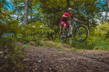 Fototapeta premium side view of young caucasian male jumping with a mountain bike over a jump on a singletrail. Epic ride with a modern mountain bike on a trail park.